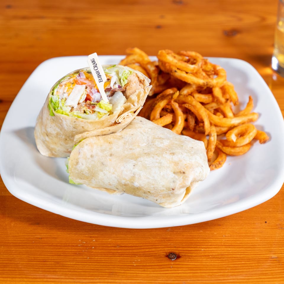 Chicken wrap with lettuce, tomato, and onion, served with a side of curly fries.