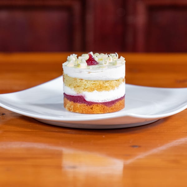 Layered dessert with white cream, yellow cake, and red fruit filling, topped with white chocolate curls.